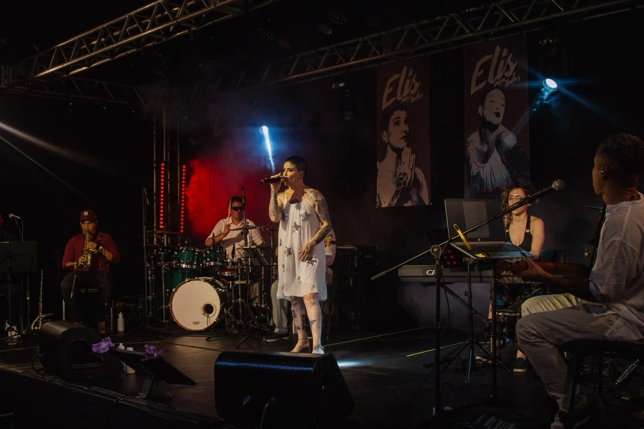 Palco iluminado e dinâmica musical com banda executando o repertório clássico da MPB